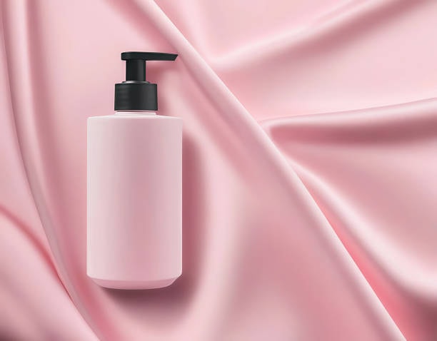 Stylish pink soap dispenser placed on pink satin fabric for luxury packaging theme