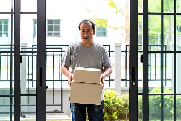 Man delivering cardboard boxes with packaged T shirts at residential entrance