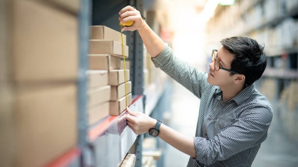 Worker measuring boxes on warehouse shelf using a measuring tape