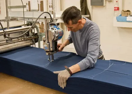 Worker using a manual handheld die cutter on stacked denim fabric