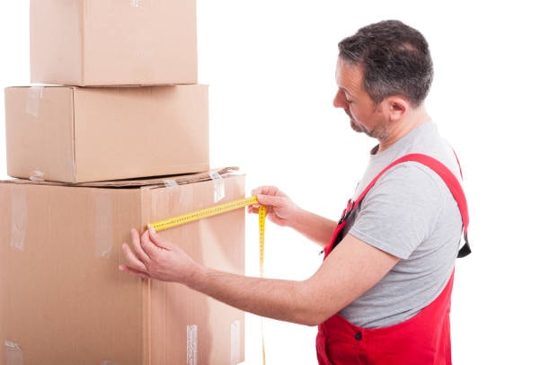 Man in red overalls measuring large stacked cardboard boxes with tape