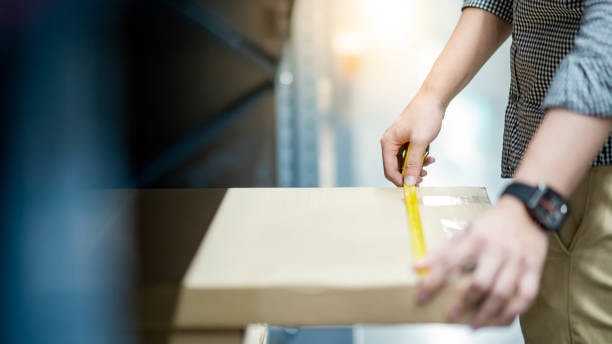 Person measuring the length of a shipping box with a yellow measuring tape
