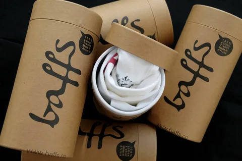 Rolled T shirt placed inside cylindrical kraft tube with black printed brand design