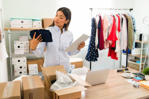 Woman inspecting folded T shirt and packing orders in home clothing studio