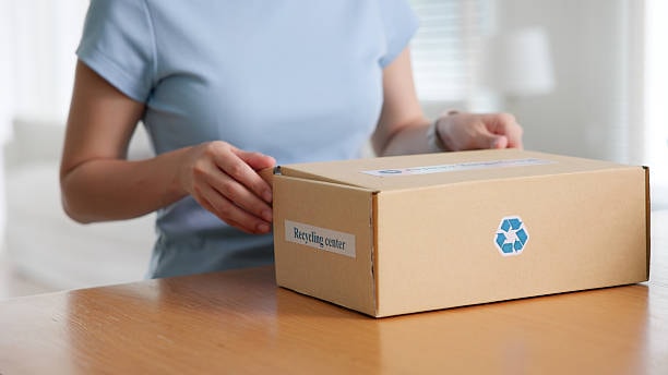 Person holding a cardboard box with recycle symbol for sustainable fashion recycling