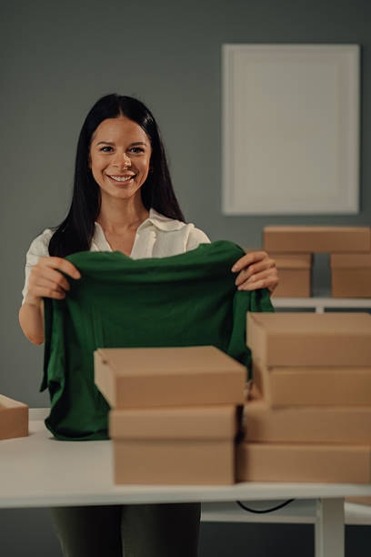 Woman preparing green T shirt for shipment with several boxes on packing table