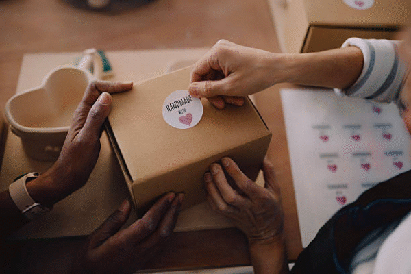 Hands applying handmade sticker on small business packaging box for personalized branding.