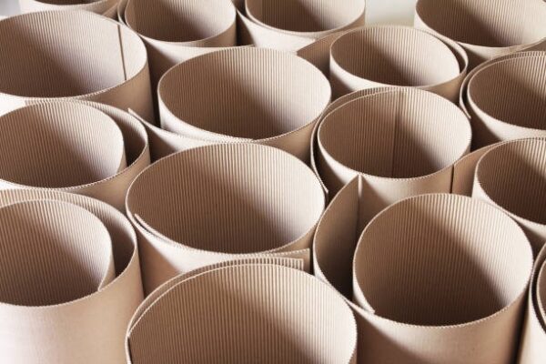 Cylindrical rolls of corrugated kraft paper arranged in rows inside a factory.