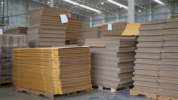 Large stacks of kraft cardboard sheets in a manufacturing warehouse ready for box production.