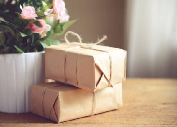 Two kraft paper wrapped boxes tied with jute string placed on a wooden table next to flowers.