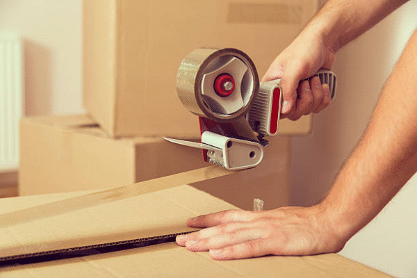 Packing a shipping box using tape dispenser for secure closure.