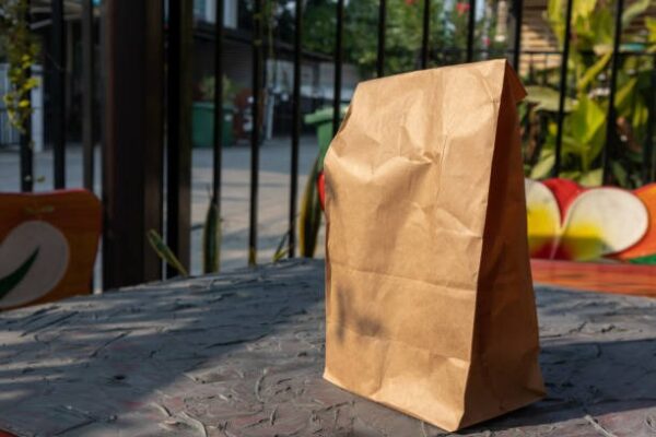 Brown kraft paper takeout bag standing upright on an outdoor café table.