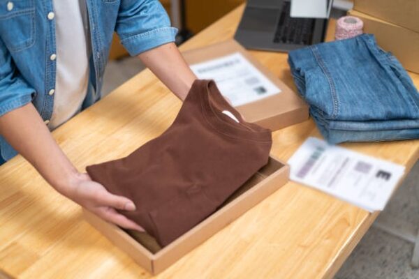 Packing a brown shirt into a custom mailer box as part of efficient e-commerce packaging for clothing brands.