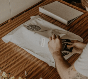 Person sealing a biodegradable mailer bag for clothing, demonstrating eco-friendly apparel packaging in fashion shipping.