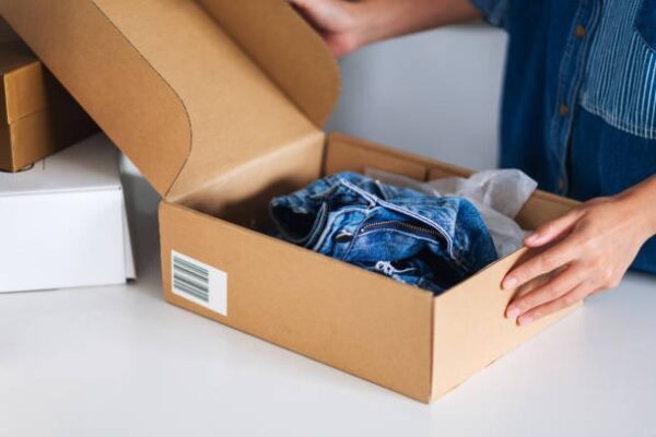 Packing jeans inside a kraft custom mailer box, showcasing sturdy and branded e-commerce clothing packaging.