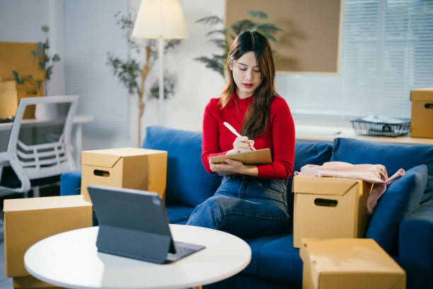 Female entrepreneur packing apparel boxes for online clothing store fulfillment.