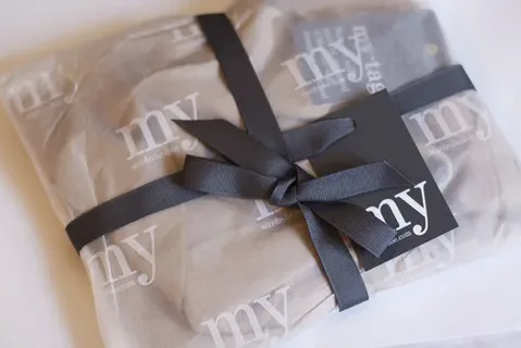 Luxury clothing packaging wrapped in tissue paper with custom logo ribbon for premium apparel presentation.