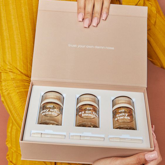 Light brown folding carton with three amber glass perfume bottles and handwritten text—showcasing sustainable packaging that uses recyclable materials and minimal design.