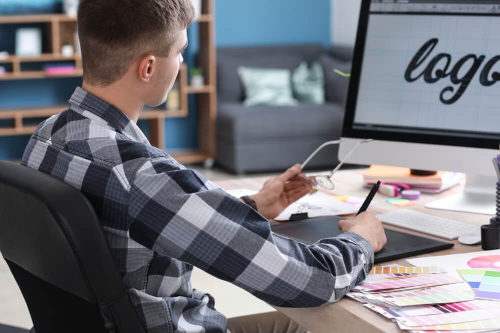 Designer working on a logo concept using a digital tablet and color swatches. This step is crucial when developing custom apparel packaging that aligns with brand values and target market expectations.