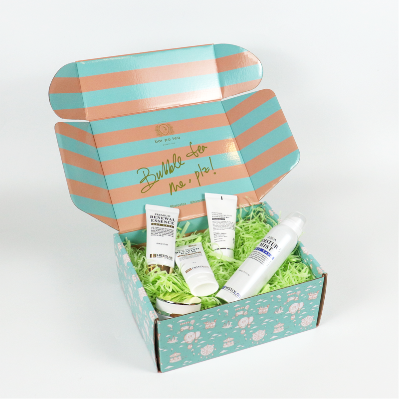 Colorful striped folding carton with green shredded paper fillers, containing multiple skincare tubes and a mist spray—designed for fun, protective e-commerce packaging.