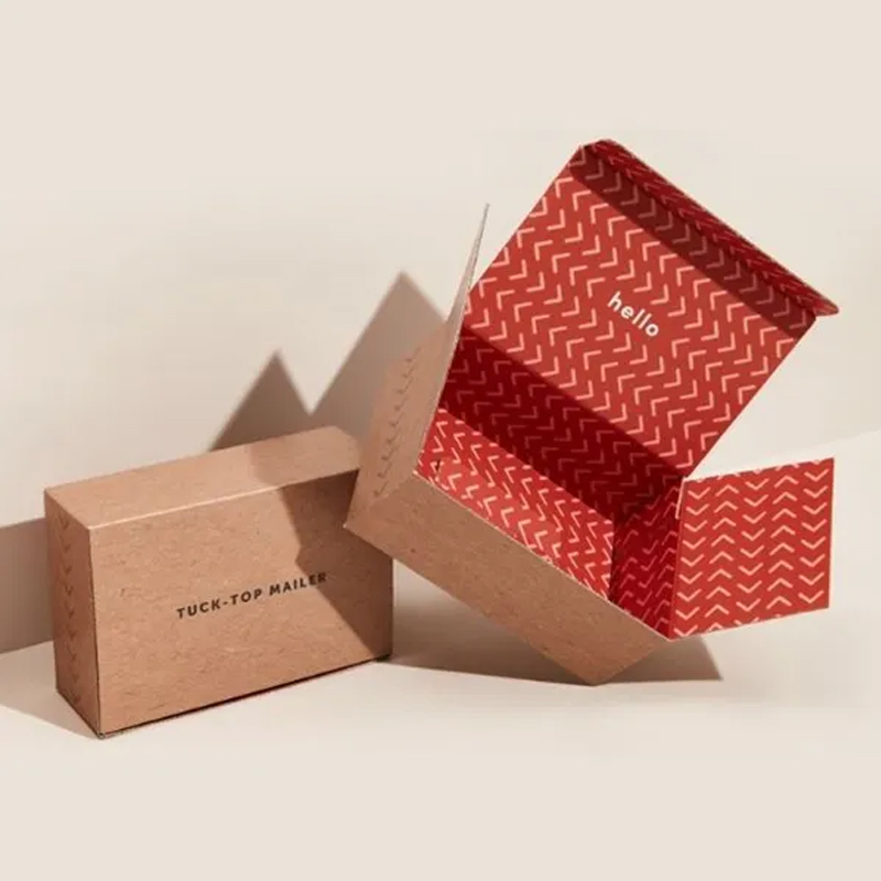 Open tuck-top mailer box with red zigzag pattern interior and "hello" text, alongside a closed brown box labeled "TUCK-TOP MAILER"—representing efficient, lightweight packaging options.