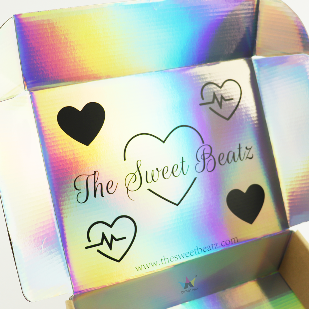 Open cardboard box featuring a rainbow holographic foil finish with black heart icons and 'The Sweet Beatz' logo, demonstrating high-contrast, eye-catching packaging ideal for e-commerce and retail.