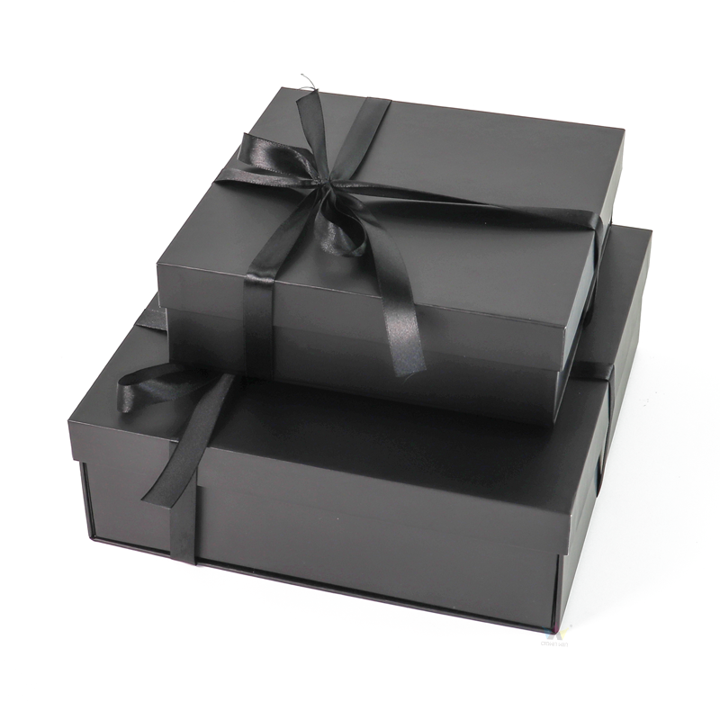 Two black rigid boxes stacked together, each tied with a black satin ribbon, showcasing elegant luxury packaging suitable for high-end clothing.