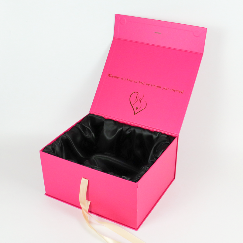 Pink rigid box with satin lining, gold foil embossing, and ribbon handle, showcasing luxury apparel packaging design.