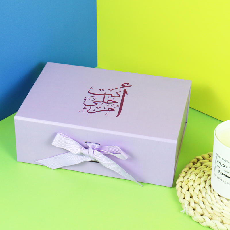 A lavender-colored rigid gift box featuring elegant Arabic calligraphy and a matching ribbon bow—showcasing culturally inspired luxury packaging with attention to detail, typography, and aesthetic harmony.