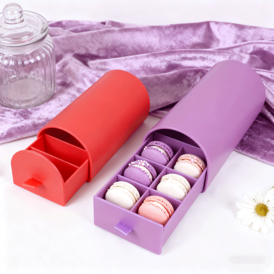Red and purple cylindrical boxes with sliding drawers containing colorful macarons, highlighting vivid color printing suitable for food packaging using either CMYK or Pantone depending on brand precision needs.
