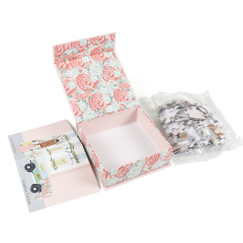 An open floral-patterned box with a matching lid, revealing an empty interior next to a sealed plastic bag of jigsaw puzzle pieces—representing playful, thematic packaging suitable for lifestyle or gift-based apparel brands.
