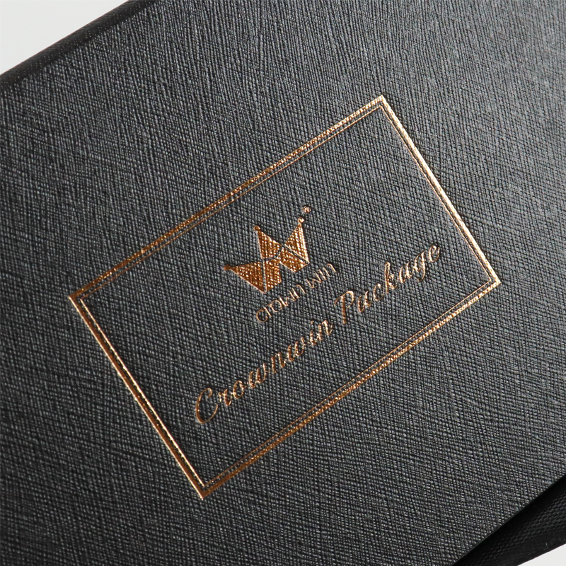 Gold foil-stamped logo and decorative border on a dark textured rigid box, featuring a crown design and elegant typography.