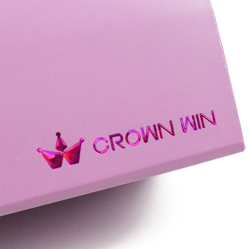 Close-up of a pink iridescent foil-stamped "CROWN WIN" logo on a glossy pink box, reflecting vibrant hues under light.