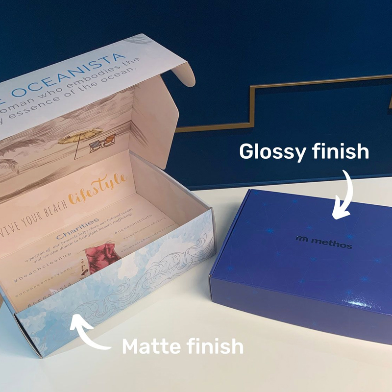 Two custom packaging boxes comparing matte and glossy finishes—one with ocean-themed artwork labeled "matte," the other a sleek blue box labeled "glossy"—highlighting surface treatment options.