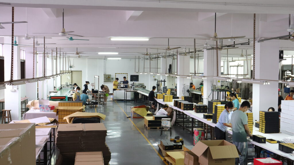 Workers assembling custom boxes in a large-scale packaging factory, showcasing the industrial environment where CMYK process colors and Pantone spot colors are used for commercial printing with high volume and brand consistency requirements.