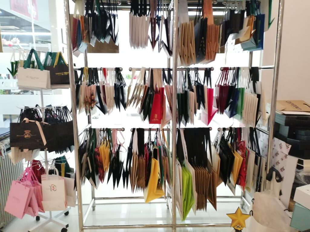 A retail showroom display featuring a wide array of colorful paper shopping bags in various sizes, colors, and finishes—highlighting custom branding options ideal for luxury or mid-tier fashion brands focusing on in-store presentation and customer engagement.