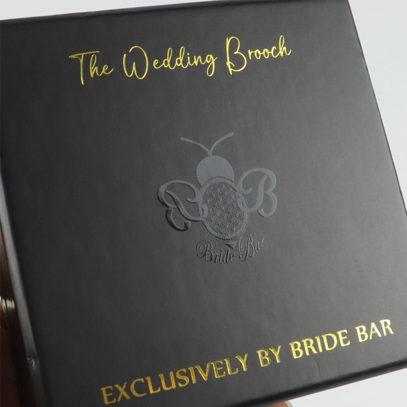 Black rigid box featuring gold Spot UV text ("The Wedding Brooch") and embossed logo with debossed details, showcasing advanced packaging techniques for high-value gift items.