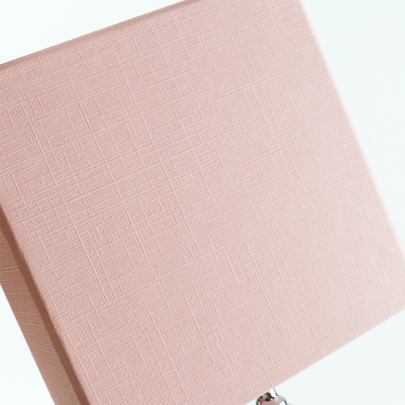 Close-up of a soft pink rigid box with a fine woven texture, showcasing the tactile quality achieved through silk screen printing on specialty paperboard.