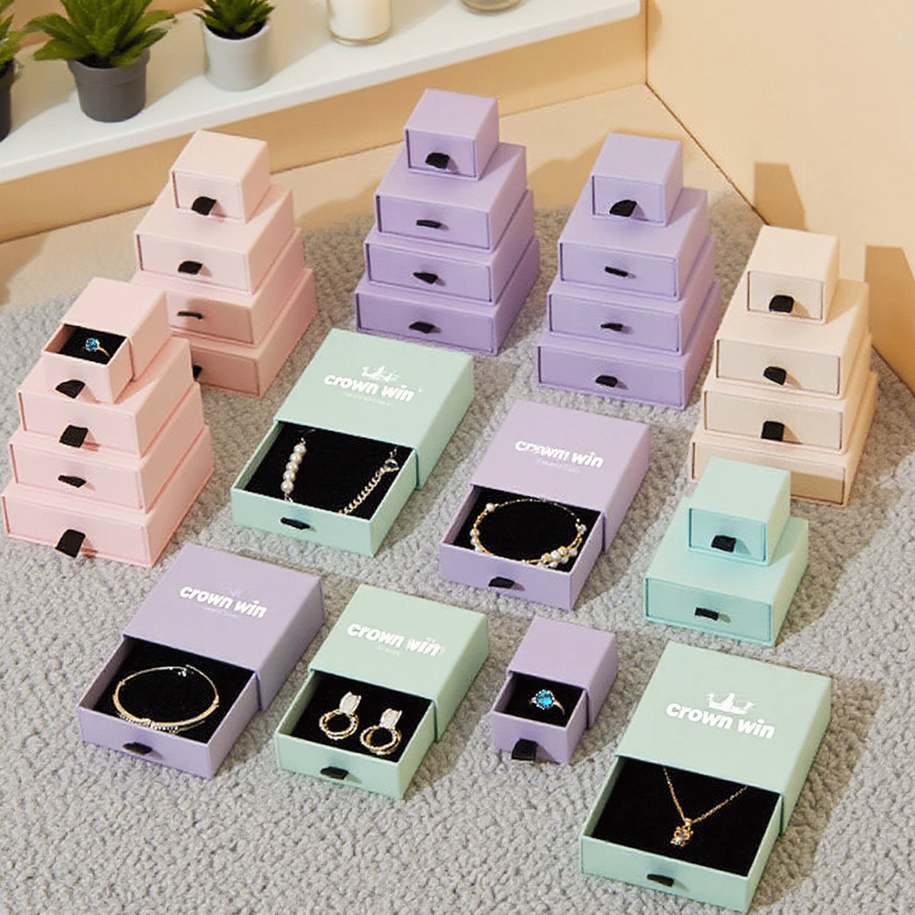 Array of pastel-colored drawer-style jewelry boxes in pink, purple, mint, and beige, featuring custom-fitted black velvet inserts holding rings, earrings, necklaces, and bracelets, showcasing consistent branding and secure product placement.