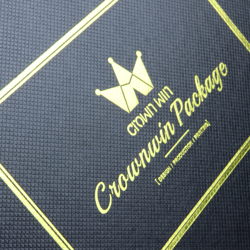 Close-up of dark blue textured surface with gold foil-stamped logo and text reading "Crown Win Package" and "Design / Production / Printing," framed by diagonal gold lines, showcasing precise registration and surface finish.