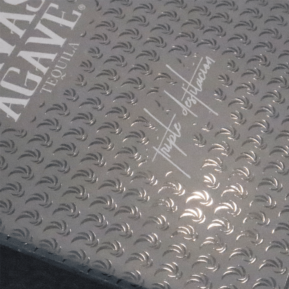 Close-up of a silver-colored box lid with embossed diamond plate texture and white text reading 'triple destillation', showcasing premium surface finishing.
