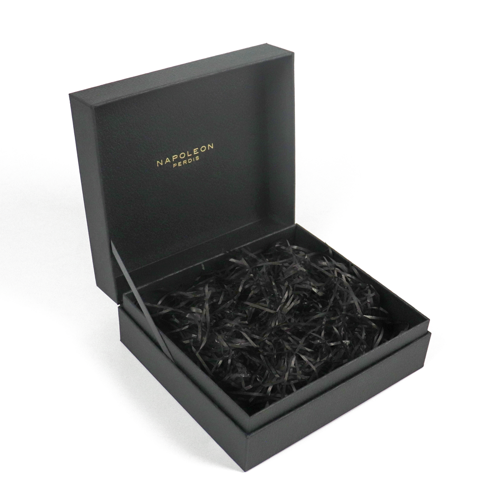 Open black box with gold foil-stamped "NAPOLEON PERDIS" on inner lid, filled with black shredded paper for cushioning.