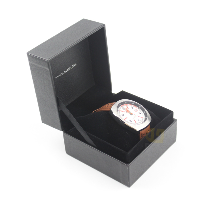 Black rigid watch box with velvet lining and embossed website text, housing a silver-tone watch with brown leather strap—designed for both protection and brand visibility.