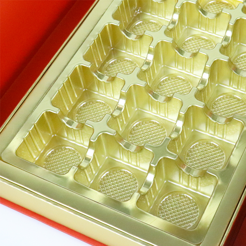 Close-up of a shiny gold metal tray with multiple compartments, each featuring textured circular bases and raised dividers, placed inside a red box.