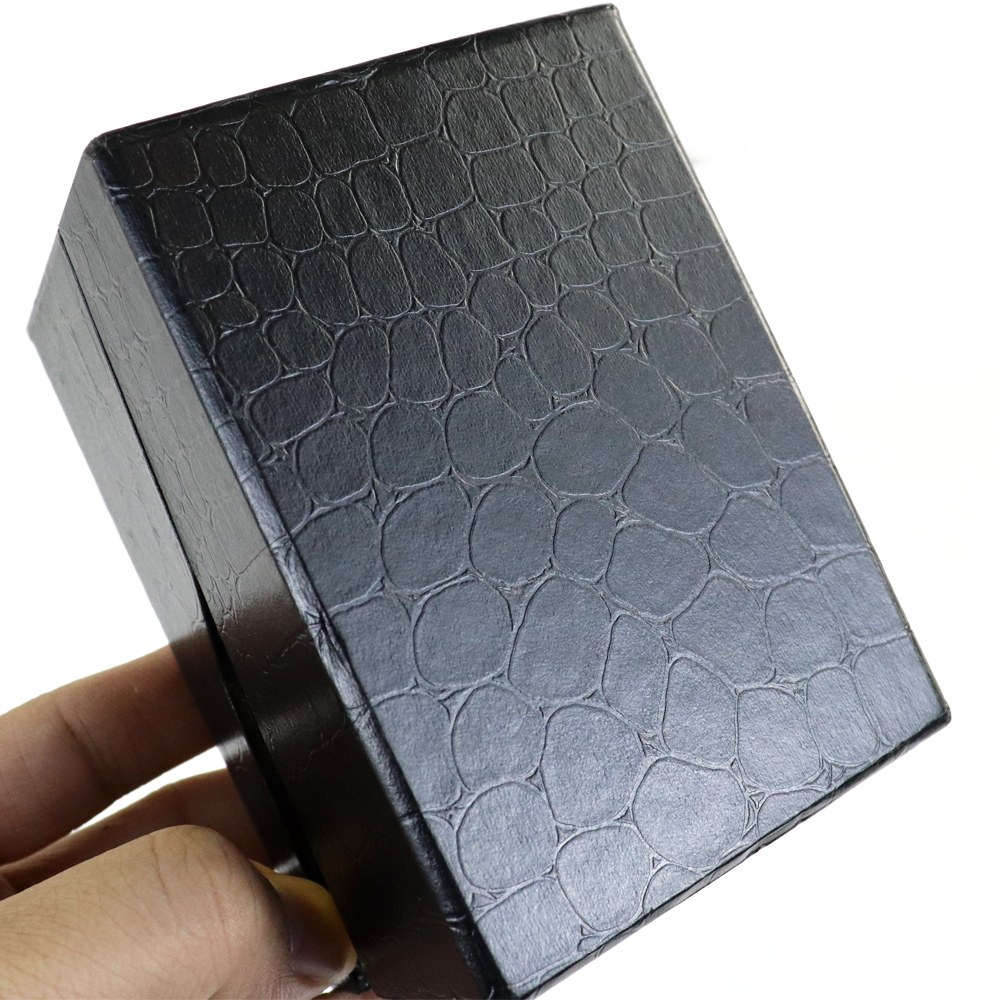 Hand holding a black rectangular box with embossed crocodile skin pattern, showcasing its size, texture, and build quality.
