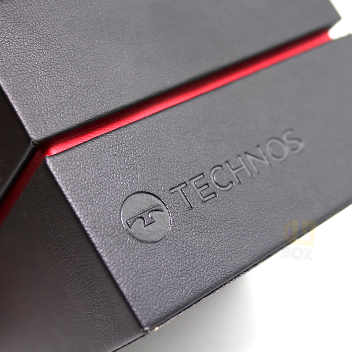 Close-up of black textured rigid box with debossed "TECHNOS" logo and red inner lining, showcasing minimalist branding with tactile refinement.