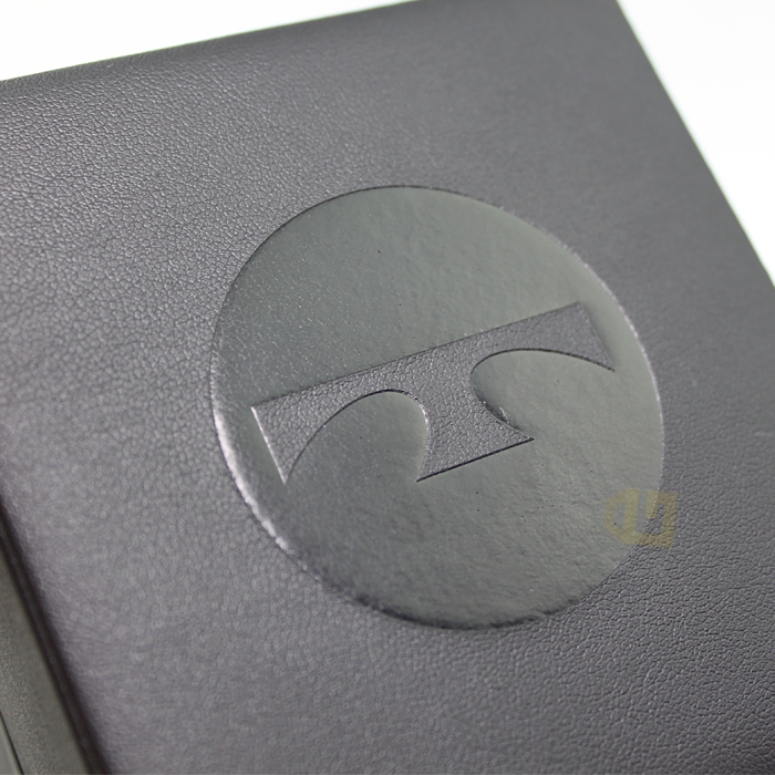 Gray leather-textured box with circular embossed logo featuring a stylized "T" symbol, demonstrating raised texture finishing.