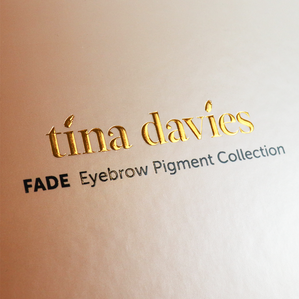 Gold foil-stamped "tina davies" logo with accent details on a warm beige background, featuring clean typography and reflective finish.