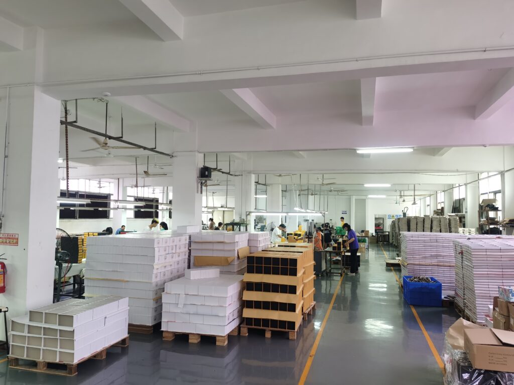 Factory floor with stacks of finished boxes and workers assembling packaging, showcasing scalable production for custom jewelry inserts.