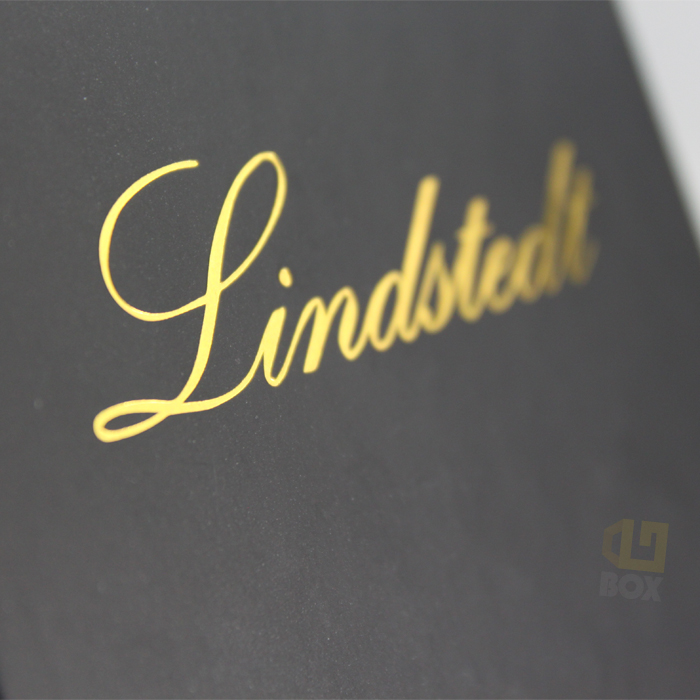 Close-up of a black matte jewelry box lid featuring gold foil-stamped cursive text "Lindstedt", showcasing sharp registration and premium contrast.